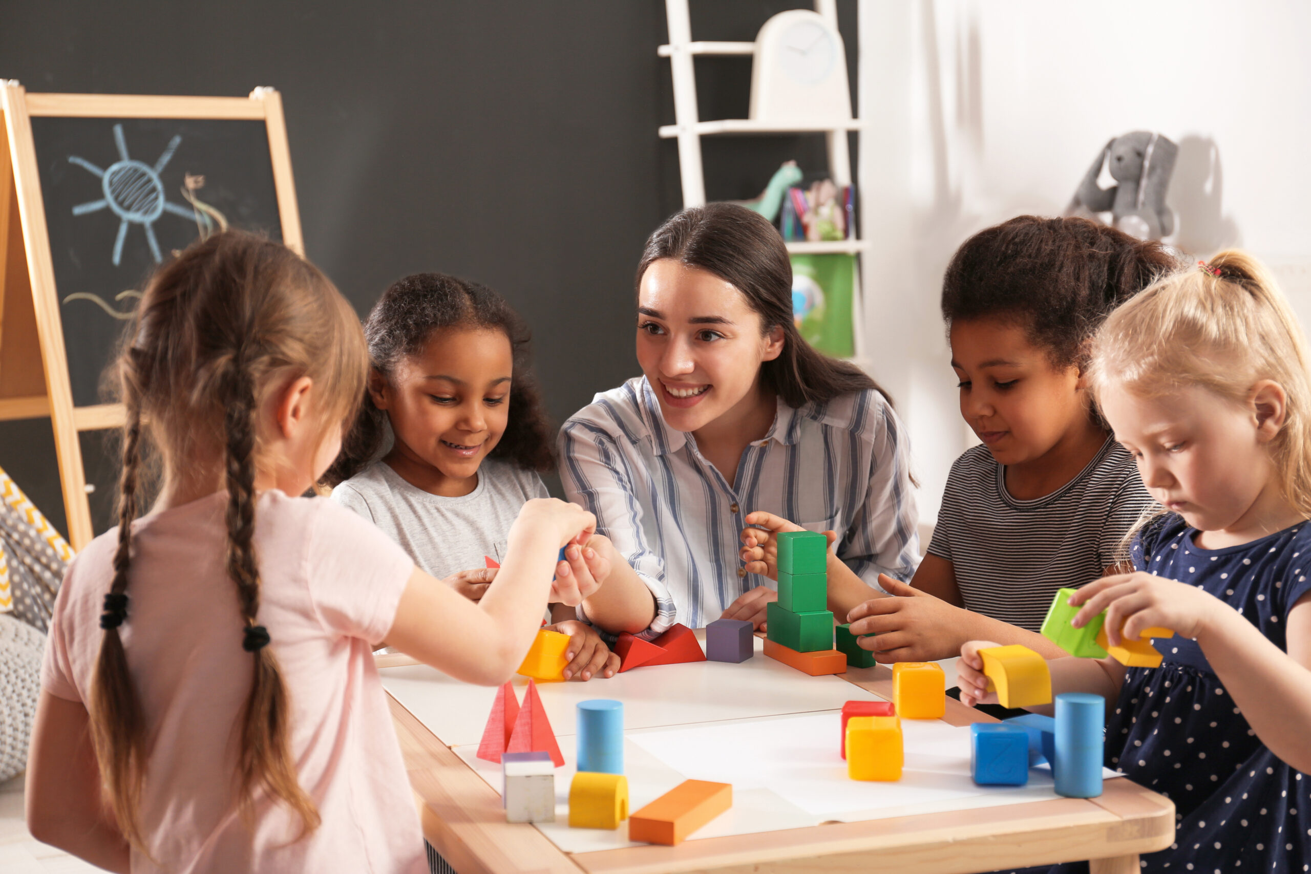 Cute little children and nursery teacher playing with building b
