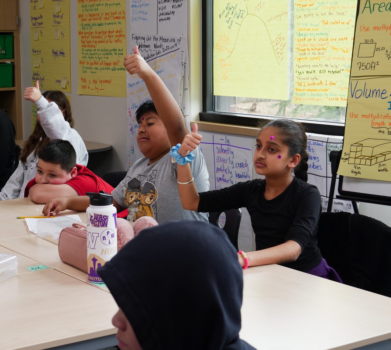 Kids in a classroom with their thumbs in the air